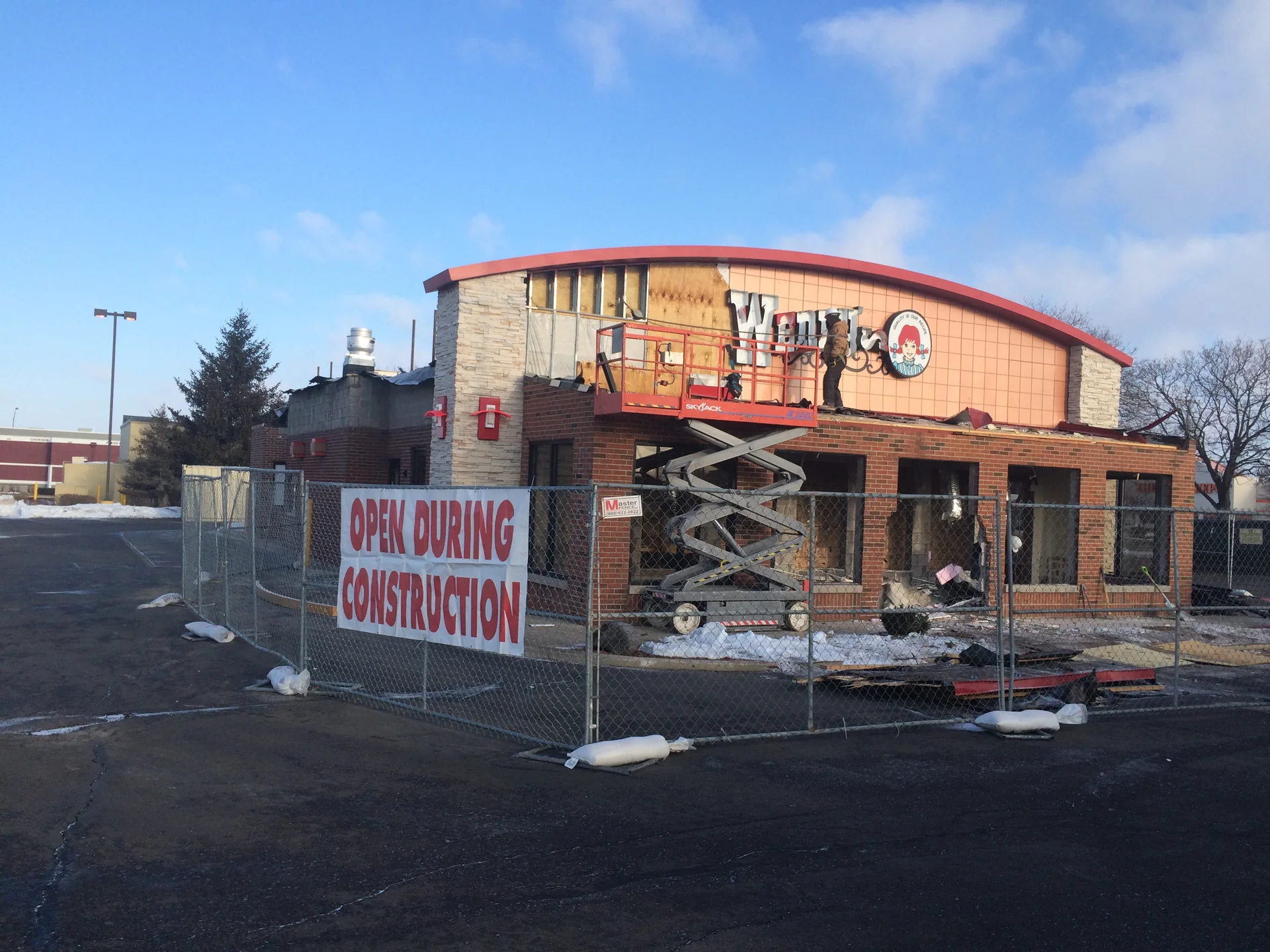 Restaurant exterior with exposed surfaces, fencing, and a scissor lift
