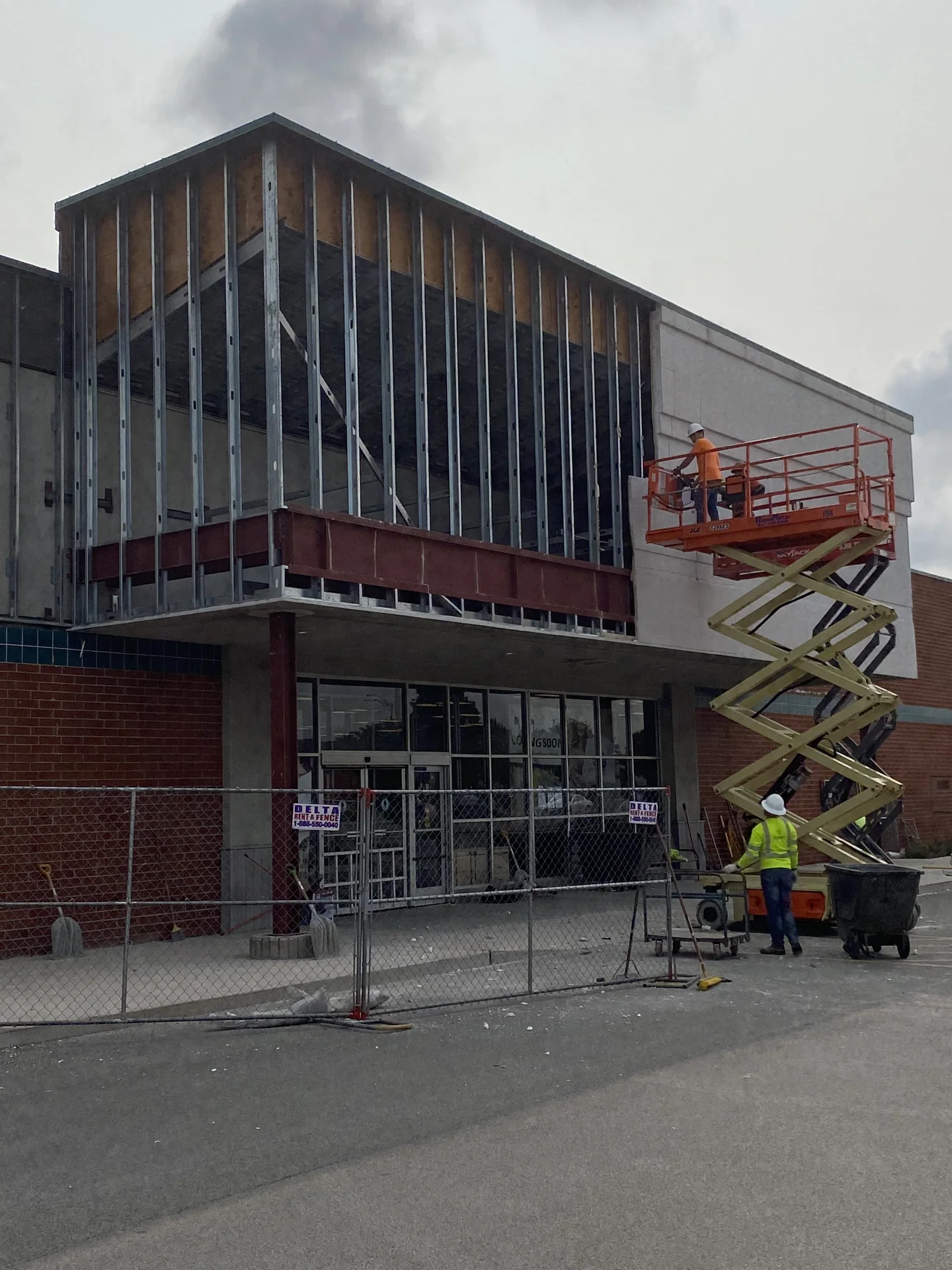 Exposed metal framing on a commercial facade with a crew and scissor lift